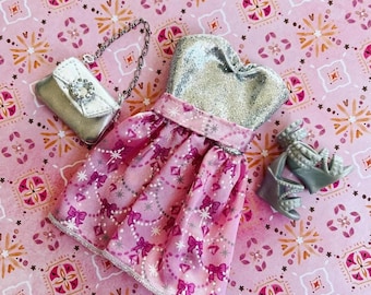 May include: A pink and silver dress with a silver glitter bodice and a pink skirt with a bow pattern. The dress is paired with silver shoes and a silver purse.