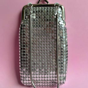 May include: A rectangular silver-toned metal mesh pouch featuring a hinged kiss-lock closure at the top. The bag is constructed from small, reflective metallic squares and includes a thin, flexible silver-toned snake chain shoulder strap.