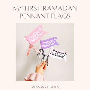 May include: Three pink, purple, and white pennant flags with the text "my first ramadan" on each. The flags are held by a hand.