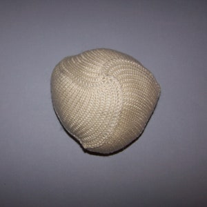 May include: A beige, knitted hat with a rounded shape. The hat is made of a textured, woven material and has a close-knit pattern. The hat is a neutral color and appears to be handmade.