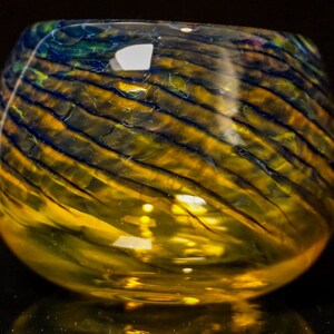 May include: A round glass bowl with a swirling pattern of blue and yellow glass. The bowl is made of clear glass and has a smooth, polished finish.