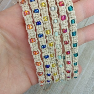 May include: Six hemp bracelets with colorful glass beads. The bracelets are woven with a macrame pattern and feature different colors of beads, including blue, green, orange, and yellow.