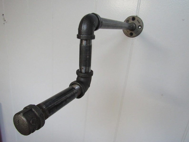 May include: Black metal pipe shelf with a 90-degree bend and a flange on the wall mount.