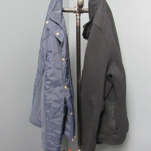 May include: A black and blue jacket hang on a metal pipe coat rack with a brown leather bag hanging below.