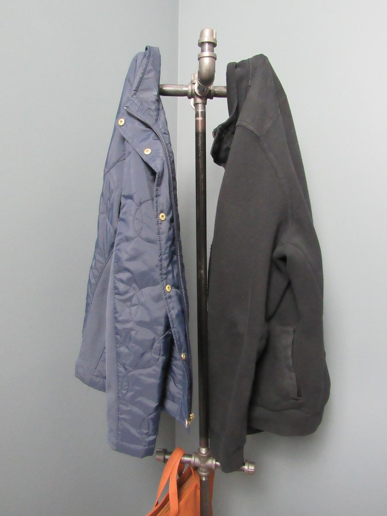 May include: A black and blue jacket hang on a metal pipe coat rack with a brown leather bag hanging below.
