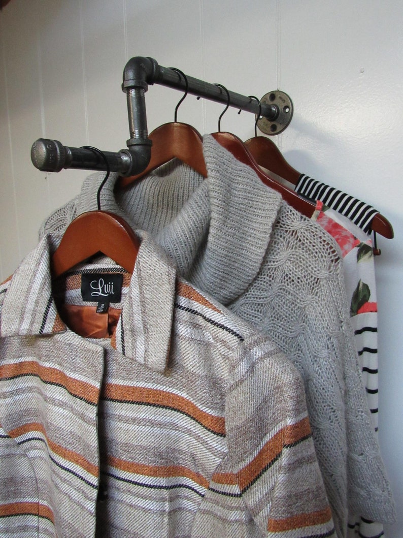 May include: A black metal pipe clothing rack with three wooden hangers holding a striped sweater, a grey knitted sweater, and a striped shirt with a "Luii" label.
