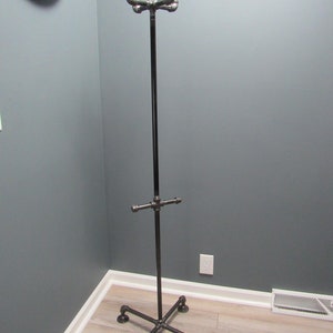 May include: A black metal coat rack with four legs and a crossbar. The rack is made of industrial pipe fittings.