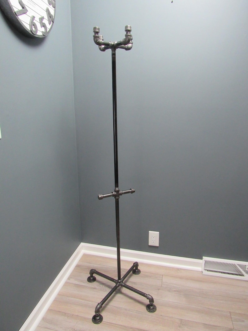 May include: A black metal coat rack with four legs and a crossbar. The rack is made of industrial pipe fittings.
