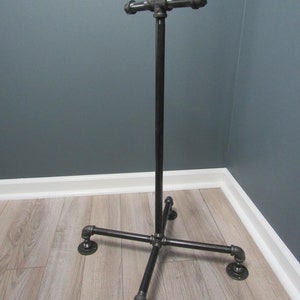 May include: A black metal coat rack with a crossbar and four legs. The rack is made of industrial pipe fittings.