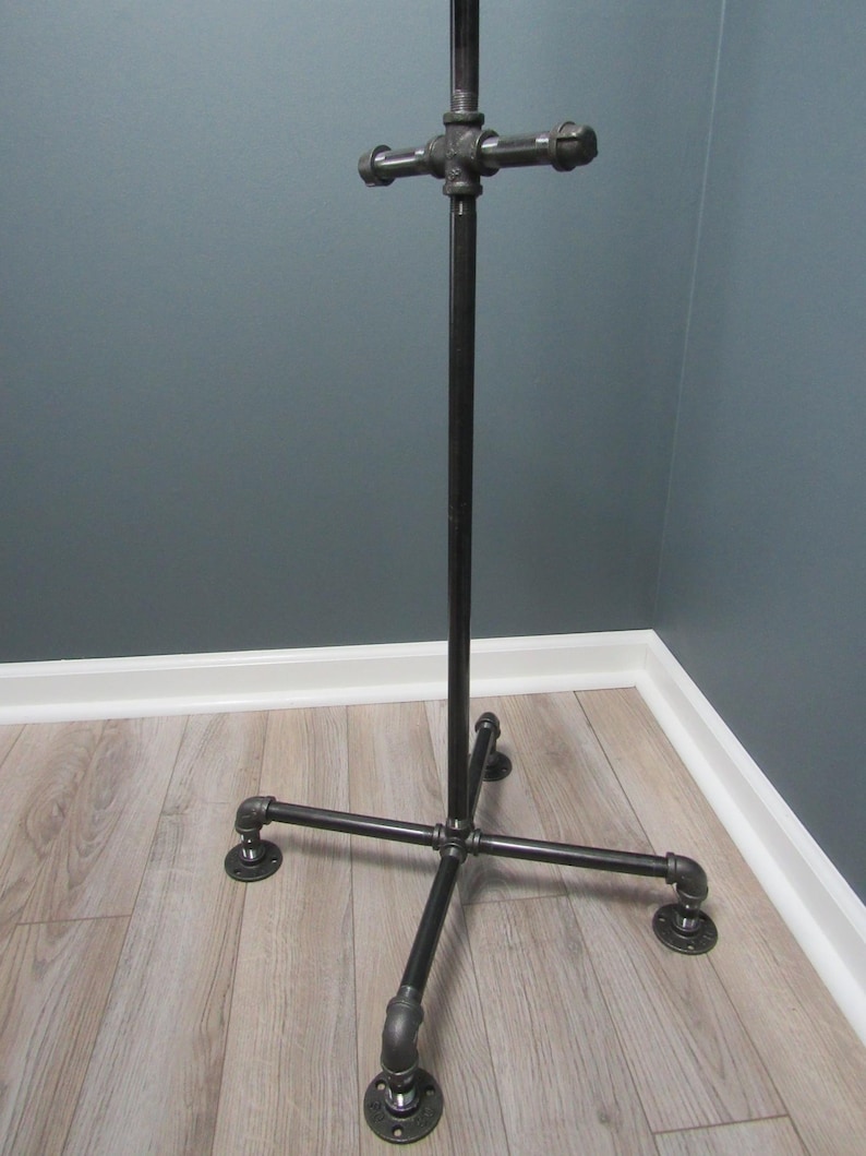 May include: A black metal coat rack with a crossbar and four legs. The rack is made of industrial pipe fittings.