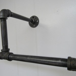 May include: Black metal pipe shelf with a 90-degree angle and a flange mounted to a white wall.