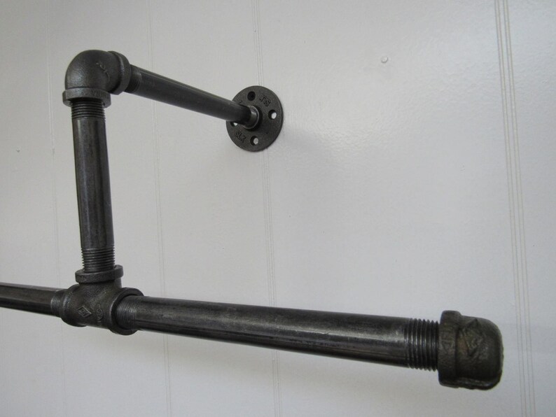May include: Black metal pipe shelf with a 90-degree angle and a flange mounted to a white wall.