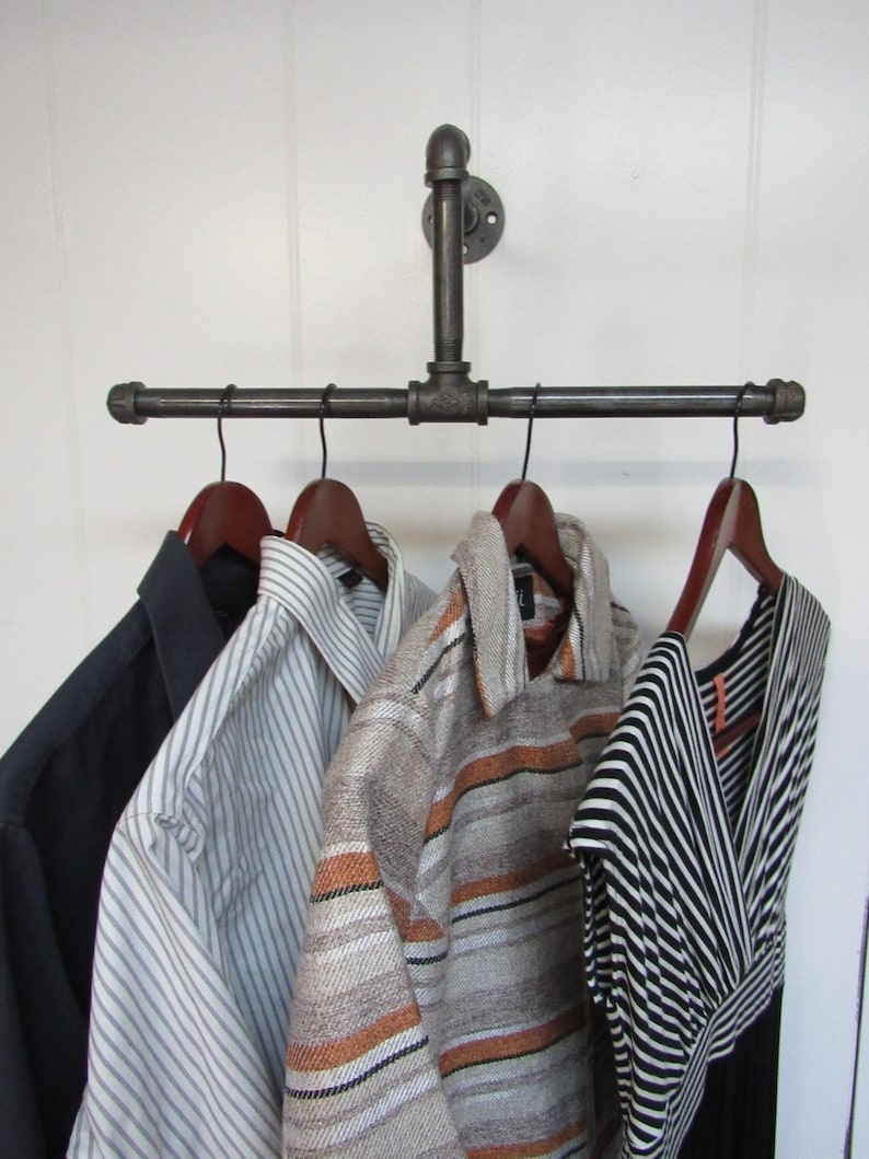 May include: A black metal pipe clothes rack with four hangers holding various clothing items, including a striped shirt, a patterned sweater, and a black and white striped dress.