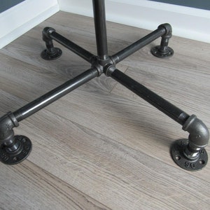 May include: Black metal pipe stand with four legs and a cross-shaped base. The stand is on a wood floor.