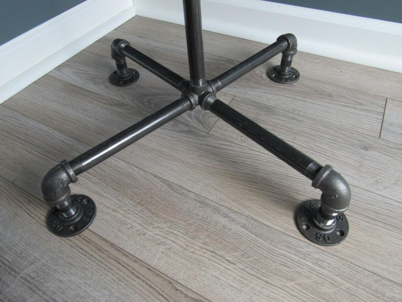 May include: Black metal pipe stand with four legs and a cross-shaped base. The stand is on a wood floor.