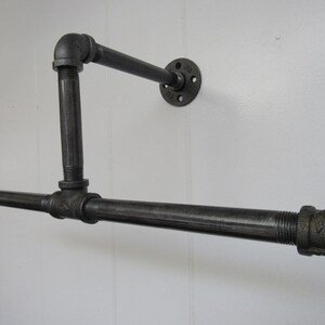 May include: Black metal pipe shelf with a horizontal bar and a vertical support. The shelf is mounted to a wall with a black metal flange.