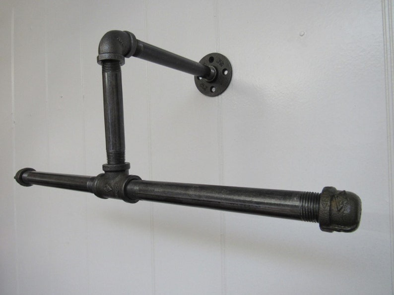 May include: Black metal pipe shelf with a horizontal bar and a vertical support. The shelf is mounted to a wall with a black metal flange.