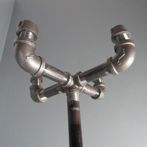 May include: A black metal coat rack with four hooks made from pipe fittings. The rack is mounted on a black metal pole.