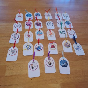 May include: A collection of white paper tags with rounded tops, each featuring a colorful circular image and a ribbon. The images include cartoon characters and various designs. Ribbons are in red, yellow, blue, and orange.