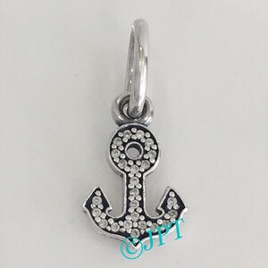 May include: A silver-colored anchor charm with a loop at the top for attaching to a bracelet or necklace. The anchor is encrusted with small, clear crystals, adding sparkle. The charm is designed with a classic anchor shape.