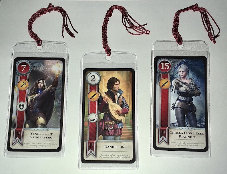 Peut inclure: Trois marque-pages lamin&eacute;s repr&eacute;sentant des personnages d'une s&eacute;rie fantastique. Chaque marque-page comporte une image de personnage, un num&eacute;ro et un nom de personnage. Les marque-pages ont des cordons rouges attach&eacute;s en haut.