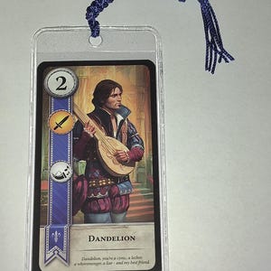 Peut inclure: Un marque-page avec une carte illustrant un homme jouant du luth, intitul&eacute; "Dandelion". La carte est dans une pochette en plastique transparent et poss&egrave;de un cordon tress&eacute; bleu attach&eacute; en haut.