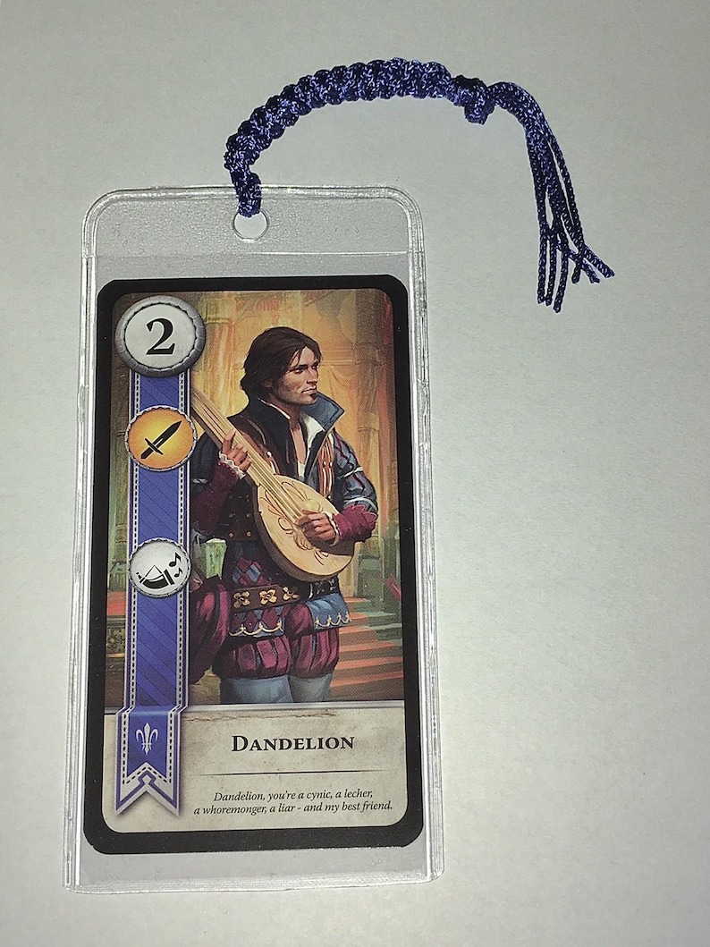 Peut inclure: Un marque-page avec une carte illustrant un homme jouant du luth, intitul&eacute; "Dandelion". La carte est dans une pochette en plastique transparent et poss&egrave;de un cordon tress&eacute; bleu attach&eacute; en haut.