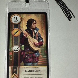 Peut inclure: Une carte repr&eacute;sentant une illustration d'un homme jouant du luth, intitul&eacute;e "Dandelion". La carte est enferm&eacute;e dans une pochette en plastique transparent avec un pompon noir attach&eacute;. La carte porte le num&eacute;ro 2 et divers symboles.