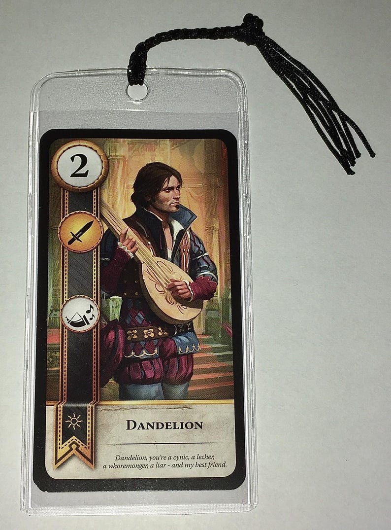 Peut inclure: Une carte repr&eacute;sentant une illustration d'un homme jouant du luth, intitul&eacute;e "Dandelion". La carte est enferm&eacute;e dans une pochette en plastique transparent avec un pompon noir attach&eacute;. La carte porte le num&eacute;ro 2 et divers symboles.