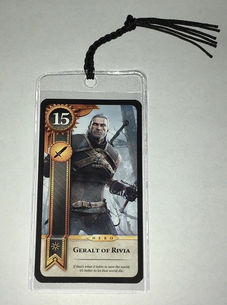 Peut inclure: Marque-page en plastique transparent avec une carte repr&eacute;sentant Geralt de Riv, personnage de la s&eacute;rie The Witcher. La carte a un bord dor&eacute;, le chiffre 15 et le texte "GERALT OF RIVIA". Une corde noire est attach&eacute;e en haut.