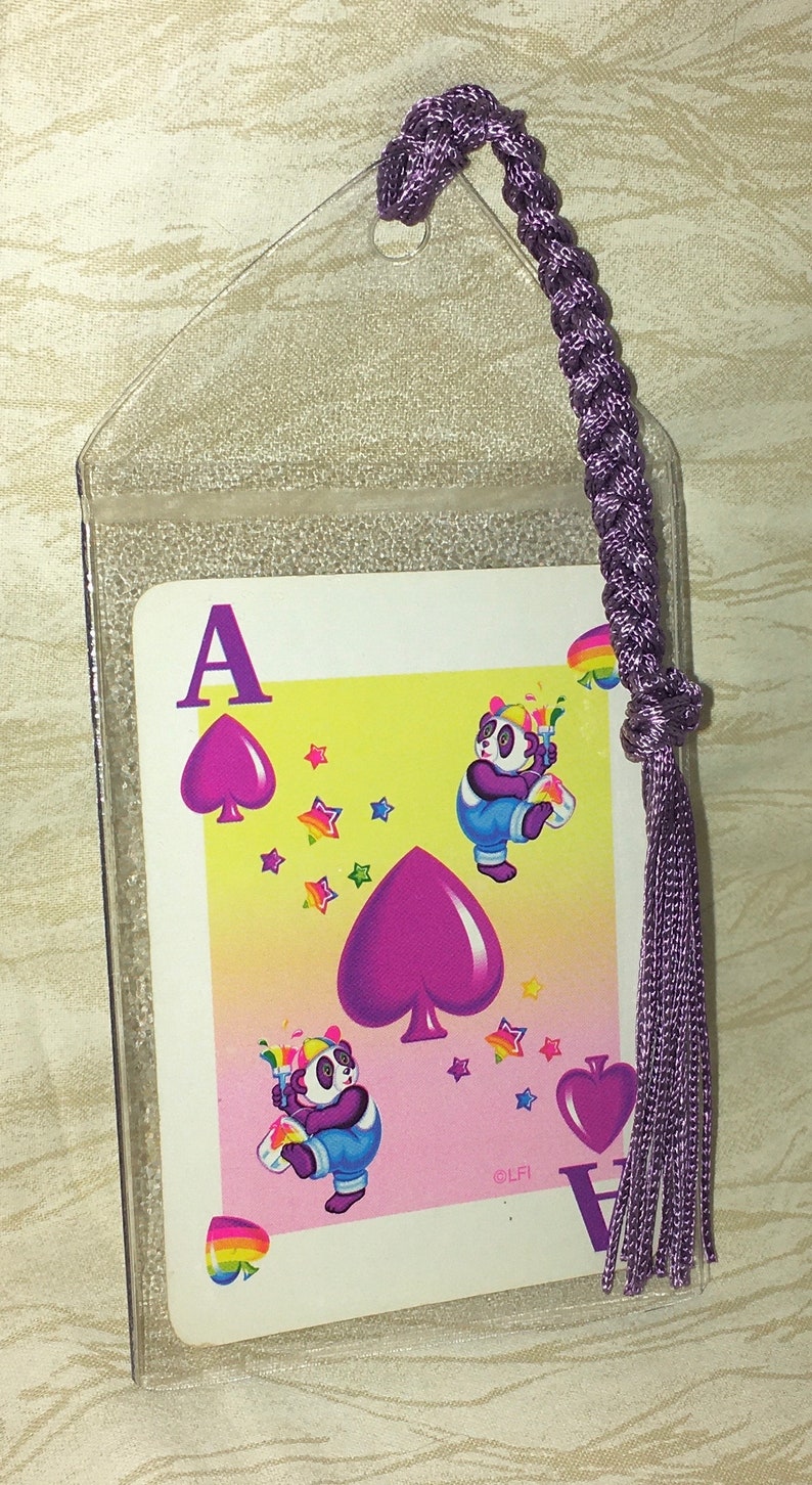 May include: A clear plastic bookmark with a playing card design. The card features a purple Ace of Spades and cartoon pandas with rainbow accents. A braided purple cord and tassel are attached.
