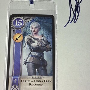Peut inclure: Un marque-page avec une carte repr&eacute;sentant une femme aux cheveux blancs en armure, avec le texte "CIRILLA FIONA ELEN RIANNON". Le marque-page a un cordon tress&eacute; bleu attach&eacute; en haut.
