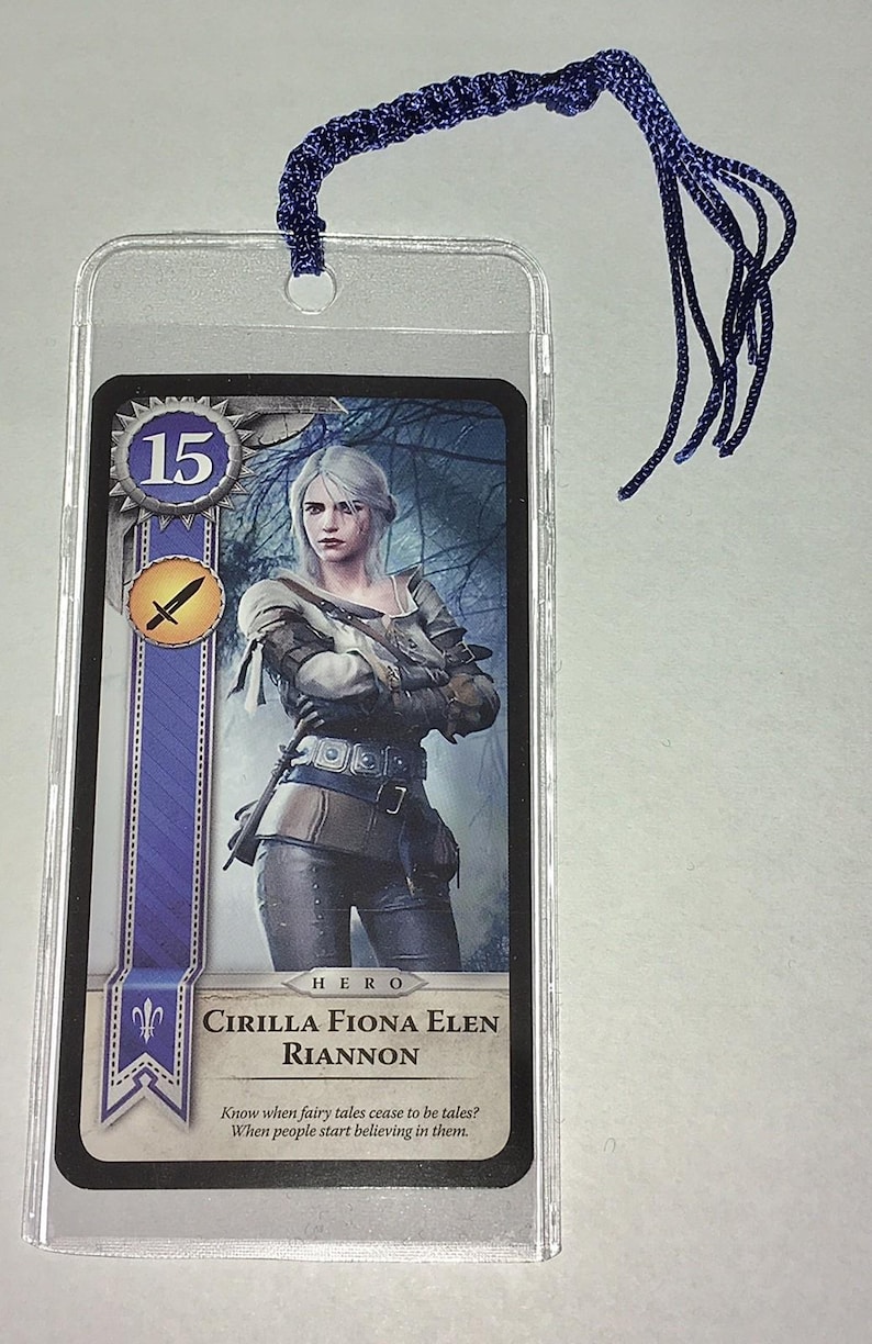 Peut inclure: Un marque-page avec une carte repr&eacute;sentant une femme aux cheveux blancs en armure, avec le texte "CIRILLA FIONA ELEN RIANNON". Le marque-page a un cordon tress&eacute; bleu attach&eacute; en haut.
