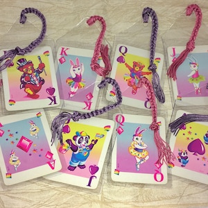 May include: A selection of playing card bookmarks, each with a cartoon animal illustration. The cards feature a bear, bunny, and panda. The bookmarks have braided tassels in pink and purple. The cards are in clear plastic sleeves.