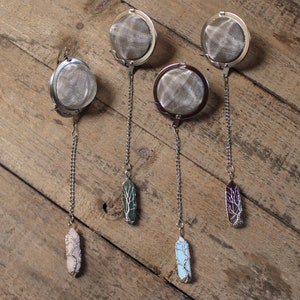 May include: Four silver tea infusers with chains and crystal charms. The charms are green, pink, blue, and purple.