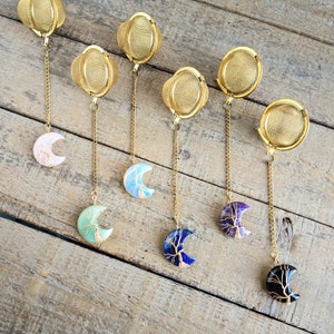 May include: Set of six gold tea infusers with different colored gemstone moon pendants. Each infuser has a fine mesh design and a chain for hanging. The pendants are made of agate, amethyst, blue lace agate, green aventurine, obsidian, and opal.