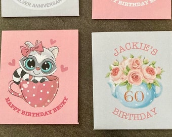 Op de afbeelding: Vijf verschillende theekop-thema kaarten met verschillende ontwerpen. De kaarten zijn allemaal wit met een licht roze of blauwe achtergrond. De eerste kaart heeft een witte theepot met bloemen en de tekst "S&P Silver Anniversary". De tweede kaart heeft een cartoonmeisje in een theekop met een wit kitten en de tekst "Happy Birthday Becky". De derde kaart heeft een cartoonwasbeer in een theekop met roze stippen en de tekst "Happy Birthday Becky". De vierde kaart heeft een blauwe theepot met roze bloemen en de tekst "Jackie's 60 Birthday". De vijfde kaart heeft een witte theepot met roze bloemen en de tekst "F&K 25 Years".