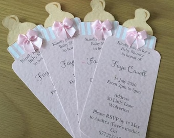Op de afbeelding: Roze en witte babyborrel uitnodigingen in de vorm van babyflesjes met een roze strik en gouden accenten. De uitnodigingen bevatten de tekst "Kindly join us for a Baby Shower in honor of Faye Cavell" en de datum en tijd van het evenement.