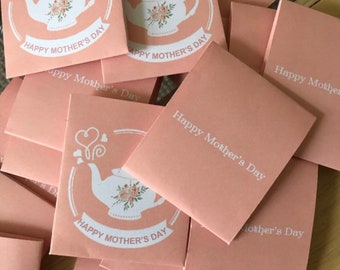 Könnte beinhalten: Ein Stapel rosa Umschläge mit einem weißen Teekannen-Design und dem Text "Happy Mother's Day".