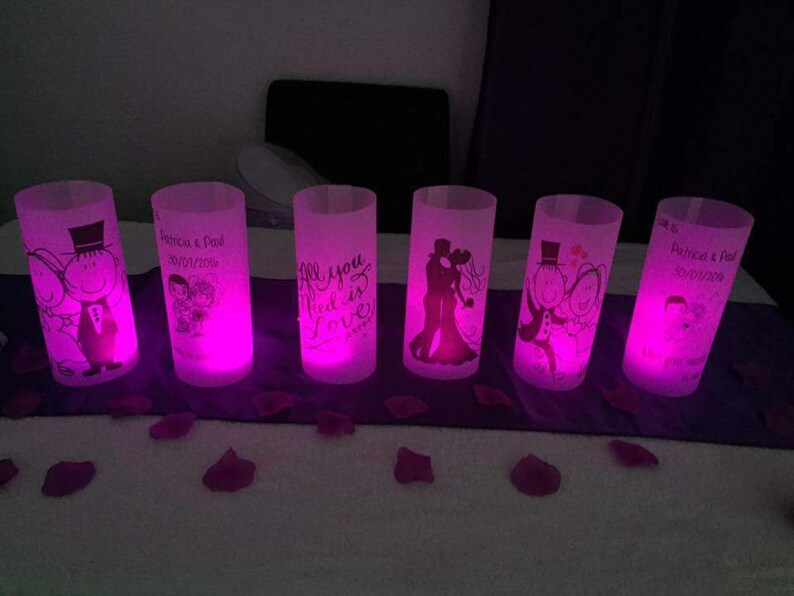 K&ouml;nnte beinhalten: Sechs klare Glaszylinder-Votivkerzenhalter mit rosa LED-Lichtern. Jeder Halter hat ein anderes Design, darunter ein Paar, eine Hochzeitstorte und den Text "Alles was du brauchst ist Liebe".