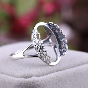 May include: Silver ring with an oval-shaped setting, featuring a delicate, intricate floral design. The setting is open, allowing for a stone to be inserted.