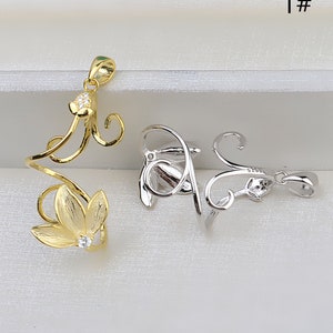 Puede incluir: Dos colgantes, uno dorado y otro plateado, en forma de flor estilizada con un diseño de espiral. Ambos colgantes tienen un pequeño cristal transparente en el centro de la flor.