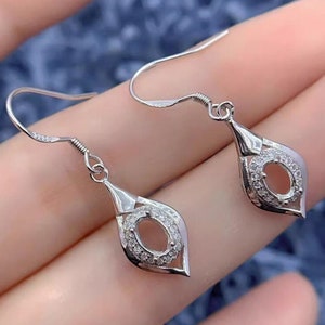 May include: A pair of silver dangle earrings with a teardrop-shaped design. Each earring features a small oval-shaped setting surrounded by smaller clear stones.