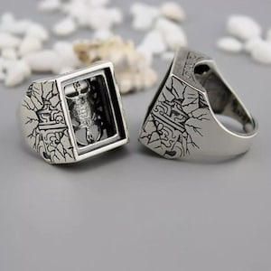 Puede incluir: Un anillo de plata con un diseño detallado de un escorpión atrapado dentro de un marco cuadrado. El anillo está hecho de plata de ley y tiene un acabado texturizado.