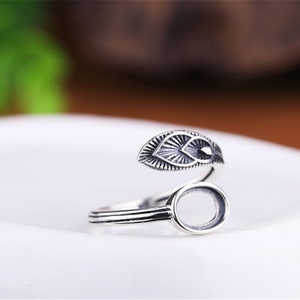 May include: Silver ring with a leaf design and an oval bezel for a stone. The ring is adjustable and can be worn on any finger.