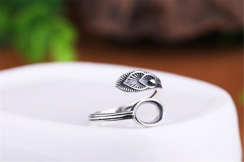 May include: Silver ring with a leaf design and an oval bezel for a stone. The ring is adjustable and can be worn on any finger.