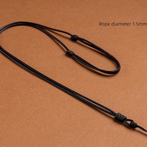 Può includere: Cordoncino nero regolabile per collana, diametro 1,5 mm. Il cordoncino è annodato in più punti per consentire la regolazione e la chiusura. Lo sfondo è di colore marrone pieno.