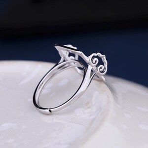 May include: A silver ring with a delicate, openwork design featuring a square shape and swirling patterns. The ring is made of metal and has a smooth, polished finish.