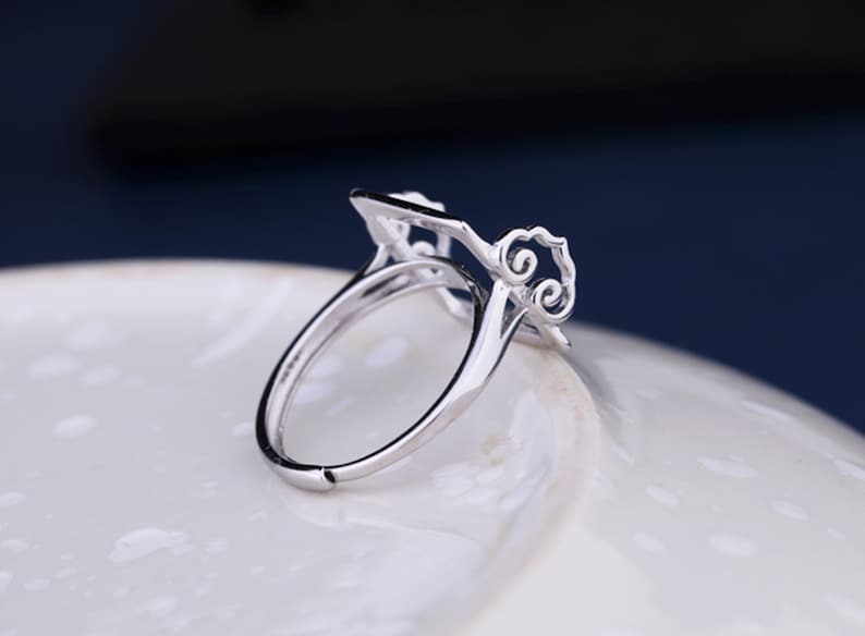 May include: A silver ring with a delicate, openwork design featuring a square shape and swirling patterns. The ring is made of metal and has a smooth, polished finish.
