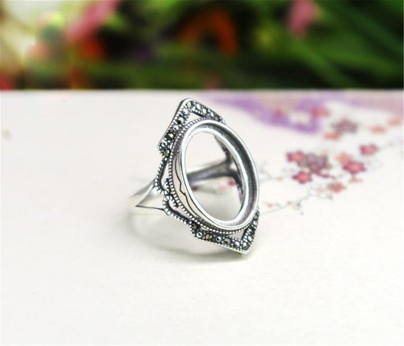 May include: Silver ring with an oval-shaped setting, surrounded by a decorative border of small black stones.